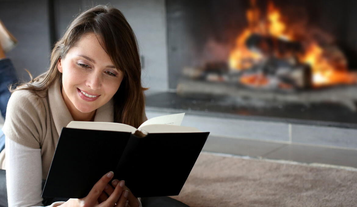 Portrait of beautiful woman reading book by fireplace